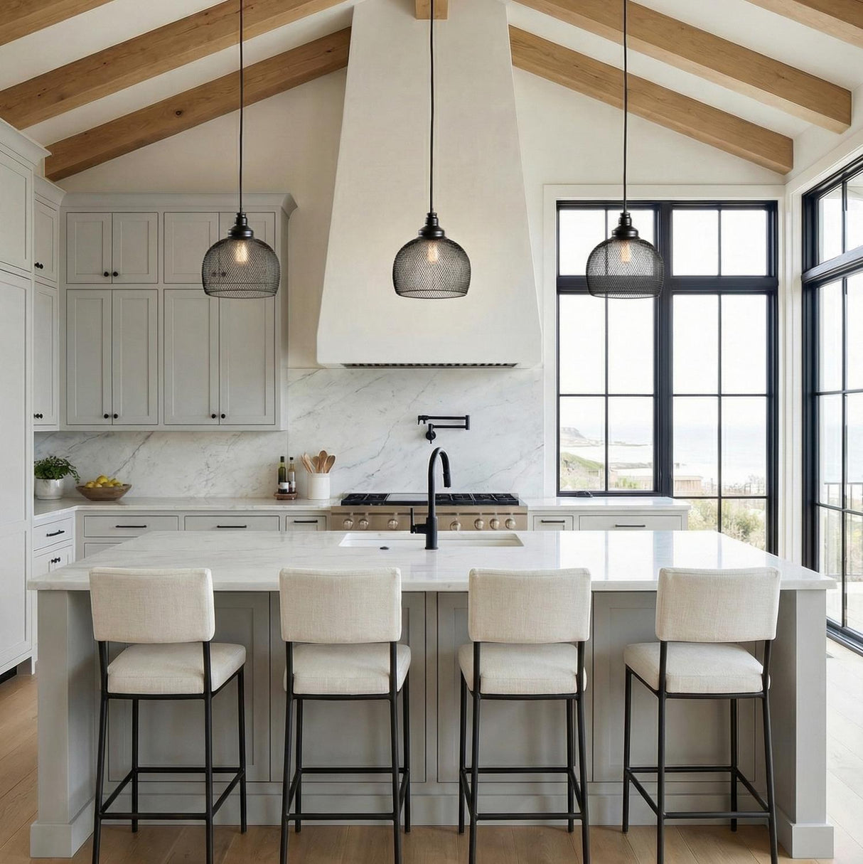 A modern farmhouse kitchen with three Bergen Bell Pendant 10 Matte Black pendants over a white marble island under a vaulted beamed ceiling and light gray cabinets.