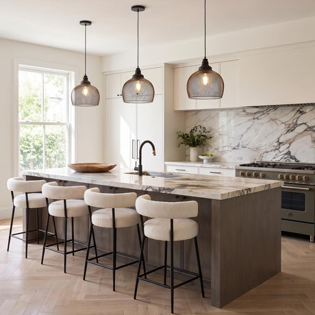 A modern kitchen with three matte black mesh pendants suspended over a white marble island featuring white boucle stools and a matching veined marble backsplash.