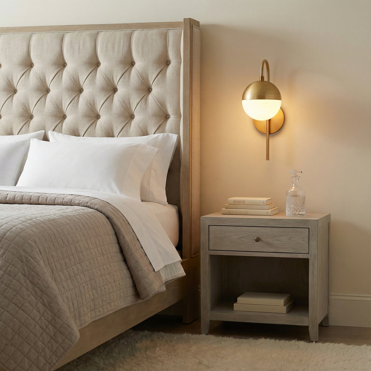 Powell Wall Sconce with Hooded White Globe, Aged Brass globe Wall Sconce in a Transitional Bedroom with tufted headboard.