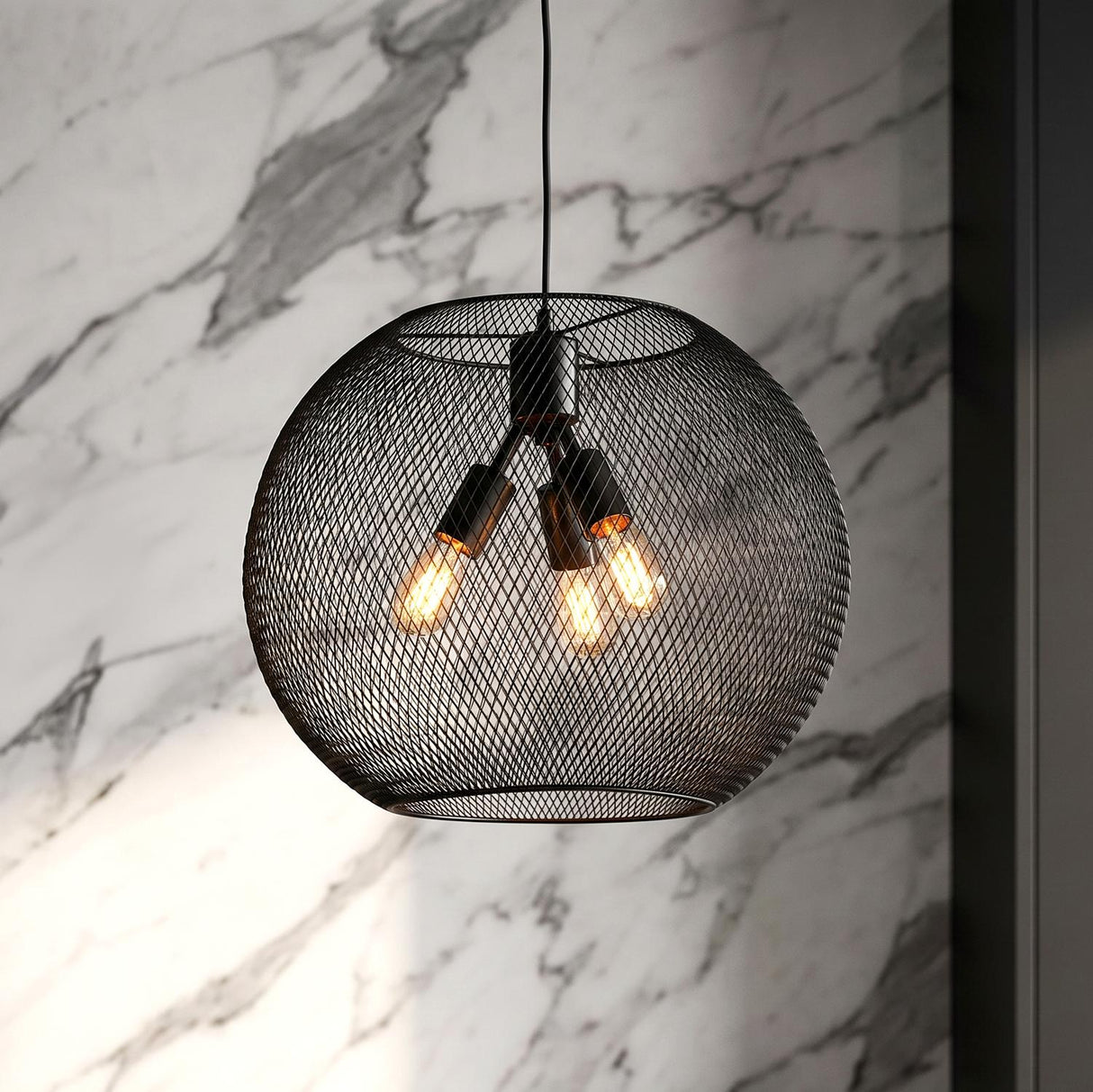 A modern kitchen with a matte black mesh globe pendant featuring three warm bulbs hanging along a white marble wall and dark cabinetry.