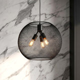 A modern kitchen with a matte black mesh globe pendant featuring three warm bulbs hanging along a white marble wall and dark cabinetry.