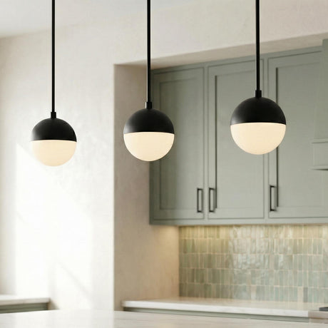 A contemporary kitchen featuring three Powell 7" Matte Black Globe Pendants with frosted glass hanging over the island near sage green cabinets and a tiled backsplash.