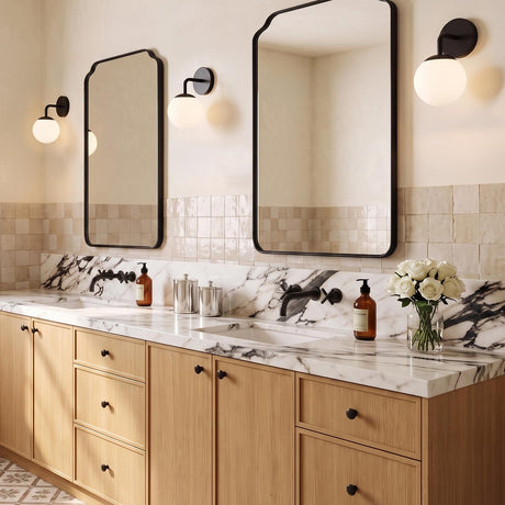 A contemporary bathroom featuring three Castell Single Globe Vanity Light, Matte Black fixtures flanking two mirrors above a marble countertop with light wood cabinetry.