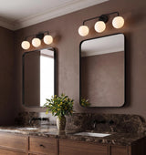 A modern bathroom with two Castell 3 Globe Vanity, Matte Black fixtures mounted above rounded mirrors over a brown marble countertop and walnut cabinets.