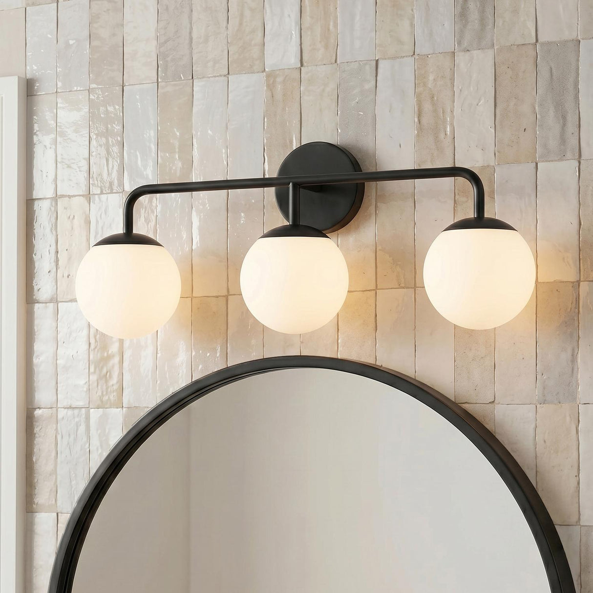 A contemporary bathroom with a matte black Castell 3 Globe Vanity with frosted glass globes mounted above a round mirror on vertical beige zellige tiles.