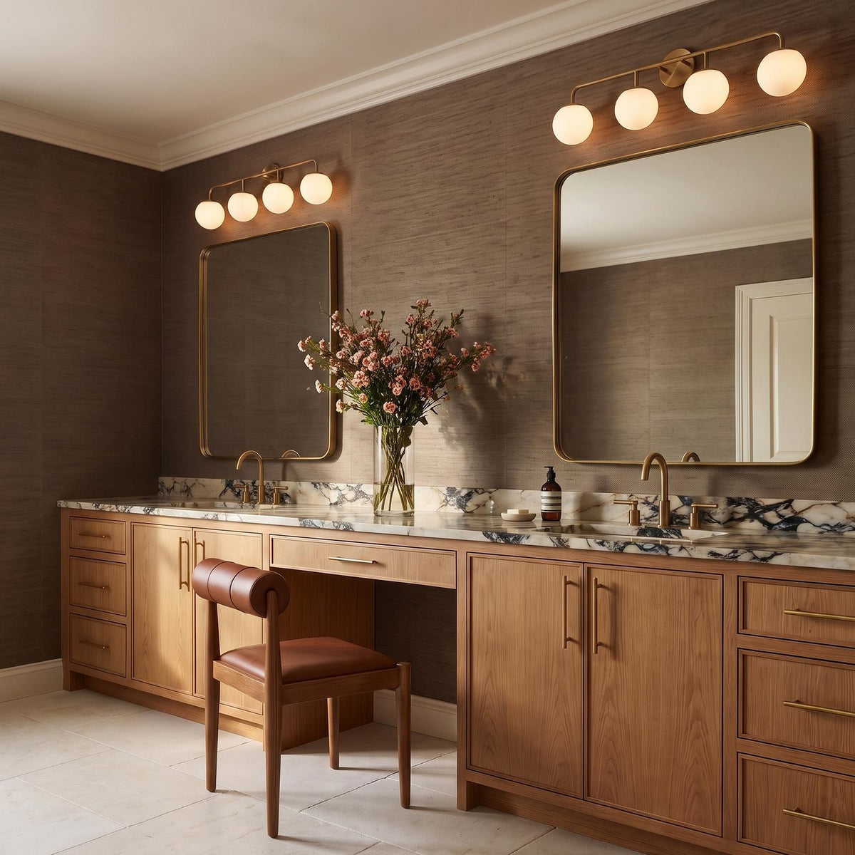 A contemporary bathroom with two Castell 4 Globe Vanity, Aged Brass fixtures mounted above rectangular mirrors, featuring light wood cabinets, marble countertops, and gold faucets.