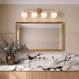 A transitional bathroom with a Castell 4 Globe Vanity in aged brass and frosted glass installed over a gold-framed mirror above a white marble countertop.