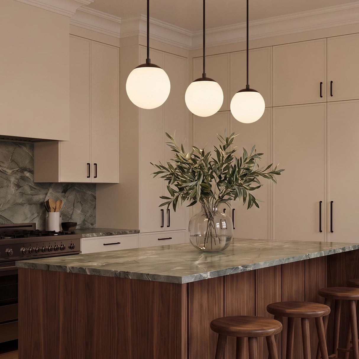 A modern kitchen with three matte black globe pendants over a walnut island with a green marble countertop and matching backsplash with beige cabinets.
