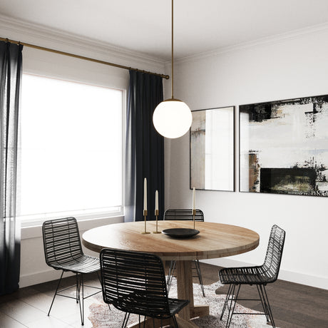 Single Castell 12" LED  Pendant Light in Aged Brass hung above a round wooden dining table with four black modern chairs and dark curtain and art