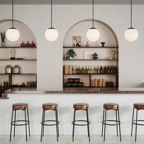 Four Castell LED 12" Globe Pendant Lights, in Matte Black hanging above a hotel bar with leather bar stools and arched shelves in the background