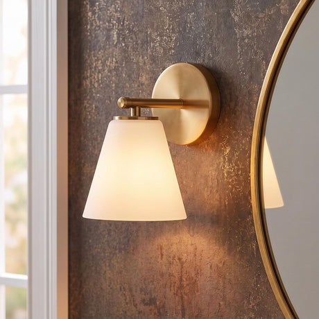 A contemporary bathroom featuring the Carlisle Vanity Wall Sconce, Brushed Brass with Opal Glass, mounted on dark textured wallpaper beside a gold round mirror.