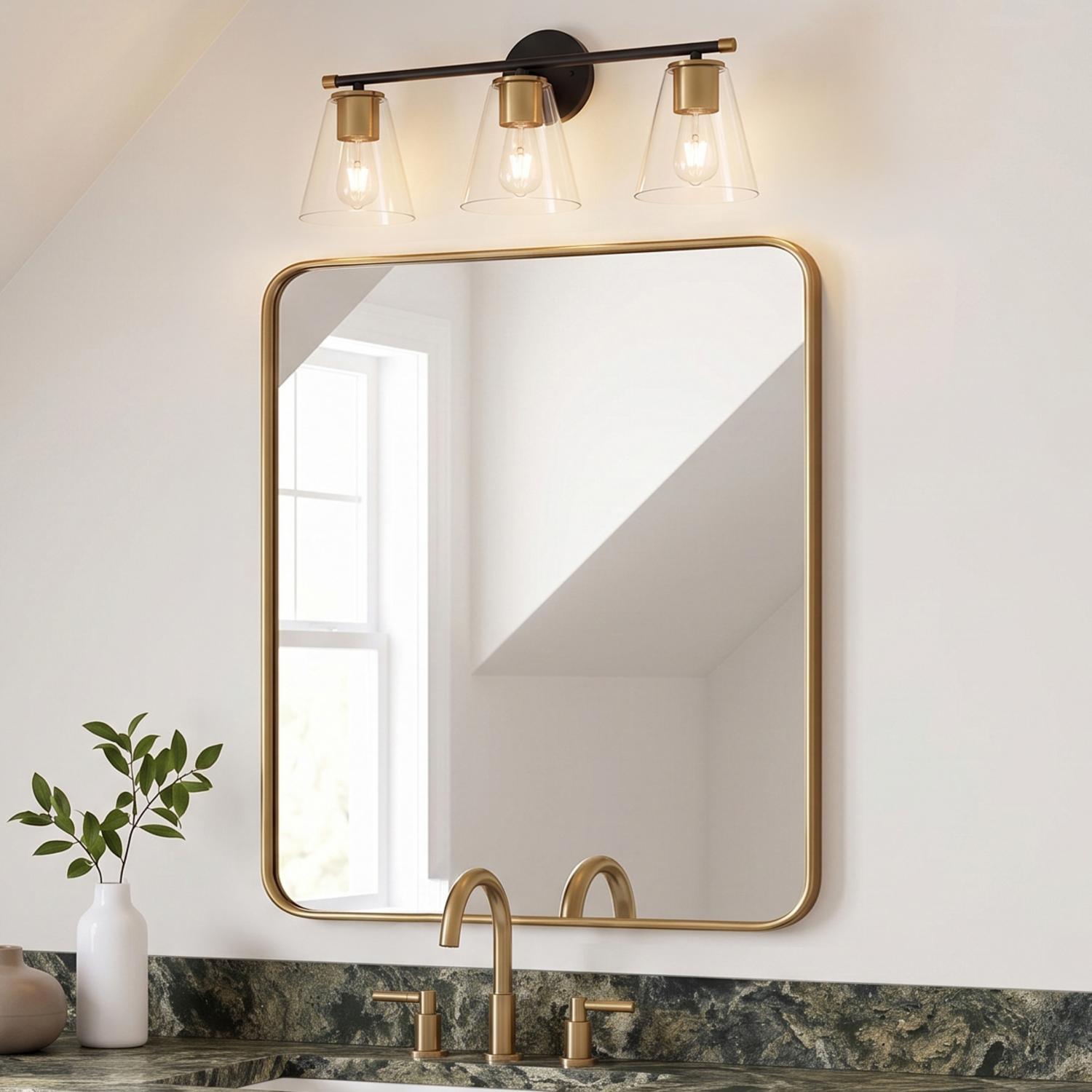 A transitional bathroom featuring the Carlisle 3 Light Vanity in matte black and brushed brass above a gold-framed mirror and green marble countertops under a sloped ceiling.