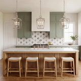 A transitional kitchen features three Anover Small Lantern Pendants in polished nickel over a light wood fluted island with sage green cabinets and floral backsplash.