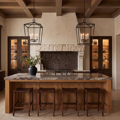 A Mediterranean kitchen with two matte black Anover Large Lantern Pendants hanging over a wood island with a grey marble countertop under a beamed wood ceiling.
