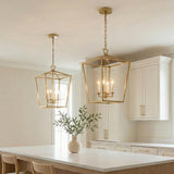 A transitional kitchen features two Anover Large Lantern Pendant 17", Satin Brass hanging over a white marble island with white cabinetry and a minimalist floral arrangement.