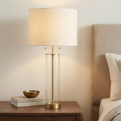Laurel Glass Cylinder Table Lamp, Satin Brass geometric Table Lamp in a Transitional Bedroom with a dark wood nightstand.