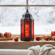 Red Glass Moroccan Christmas Lantern with twinkle lights for modern red and black holiday decor, shown in a winter window sill