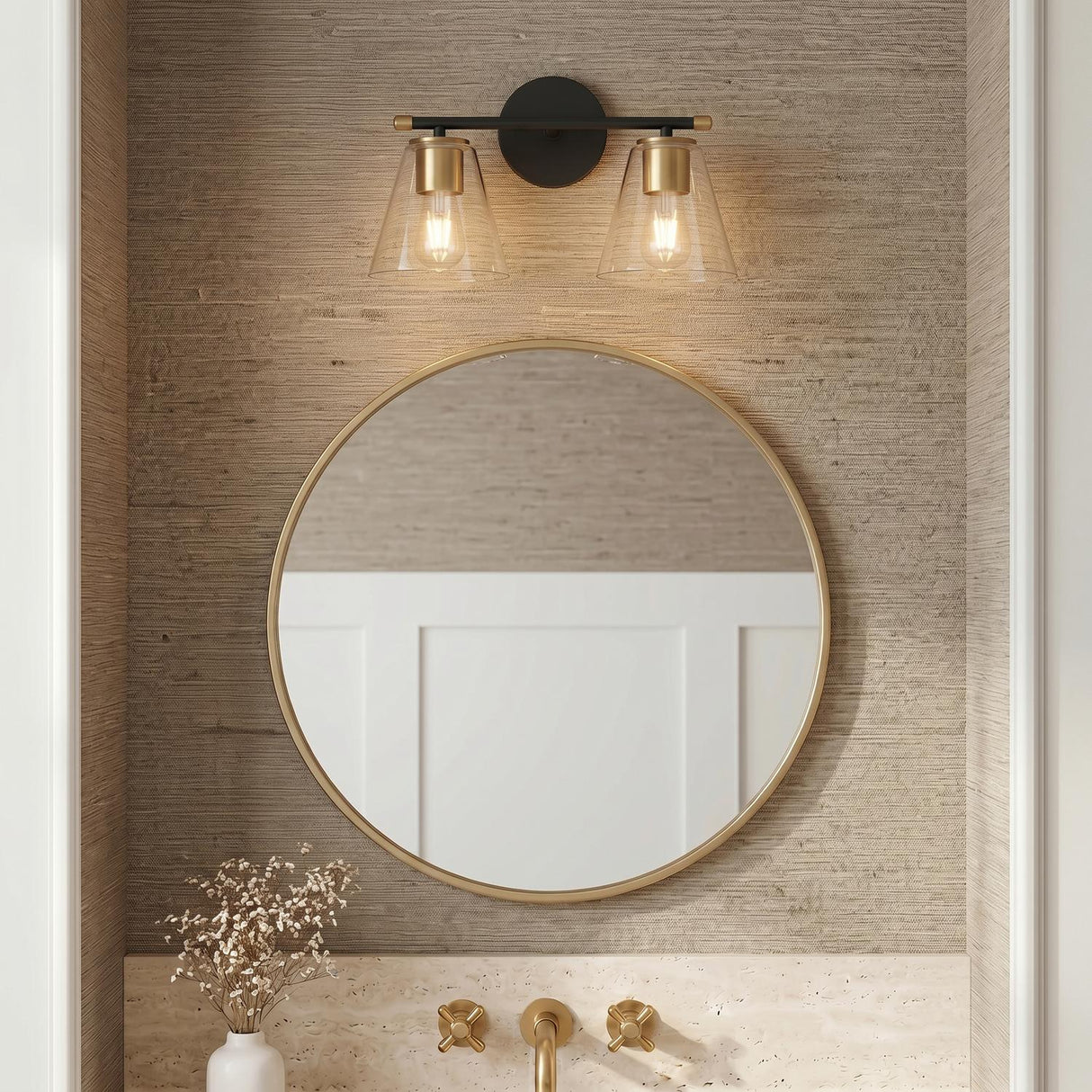 A transitional bathroom with the Carlisle 2 Light Vanity in matte black and brushed brass above a round gold mirror and textured beige grasscloth wallpaper.