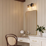 A modern farmhouse bathroom with a Carlisle 2 Light Vanity in matte black and brushed brass mounted above a gold-framed mirror and beige shiplap walls.
