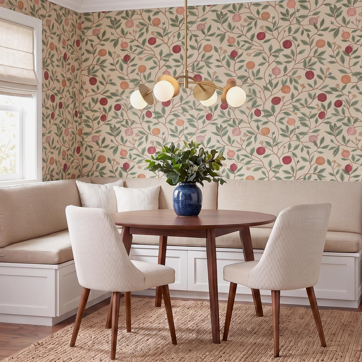 A cottage dining room featuring the Levi 4 Globe Chandelier in aged brass over a round mahogany table and cream banquette with botanical pomegranate wallpaper.