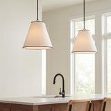 A transitional kitchen with two Luca Large 18-inch Conical Pendants in matte black and linen over a white marble island with walnut cabinets and a black faucet.