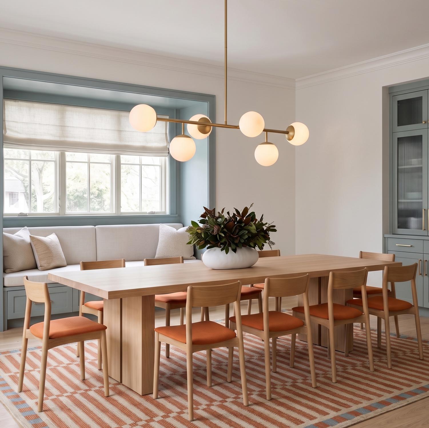 A contemporary dining room with the Castell 6 Globe Linear Pendant in aged brass over a light wood table with orange chairs and blue-green cabinets.