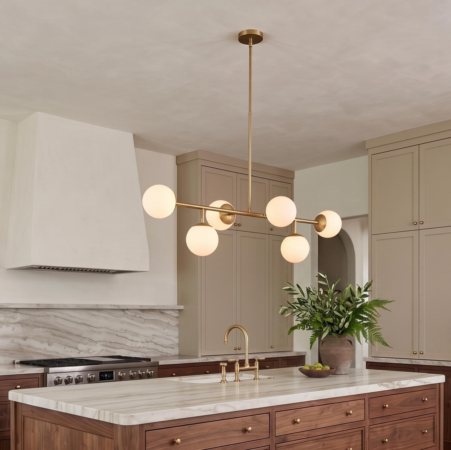 A contemporary kitchen featuring the Castell 6 Globe Linear Pendant in aged brass with frosted glass globes over a marble topped walnut island and taupe cabinets.