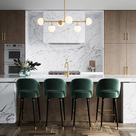 Castell 6 Globe Linear Mid-Century Modern LED Pendant, Aged Brass Finish with Opal White Glass Globes, shown in a modern kitchen with a white marble backsplash and walnut cabinets, aged brass hardware, and dark green velvet counter stools.