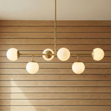 Castell 6 Globe Linear Pendant 46", Aged Brass globe linear Pendant in a Mid-Century Dining Room with a light wood slat wall.