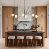 A modern kitchen with three Castell 2 Globe Pendants in matte black and aged brass above a dark stone island with a marble slab backsplash.