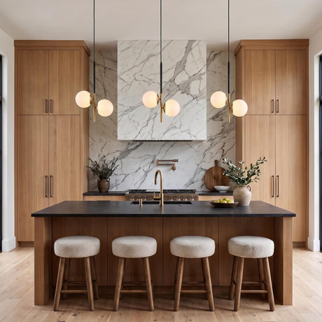 A modern kitchen with three Castell 2 Globe Pendants in matte black and aged brass above a dark stone island with a marble slab backsplash.