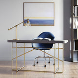 Modern office desk with gold frame, blue chair, and the Owen table lamp in satin brass finish in a room with a painting on the wall.