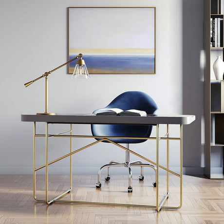 Modern office desk with gold frame, blue chair, and the Owen table lamp in satin brass finish in a room with a painting on the wall.