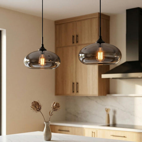 A modern kitchen with two matte black Greenwood Pendant 11" with Mirrored Smoke Glass fixtures hanging over the island beside light wood cabinets and a marble backsplash.