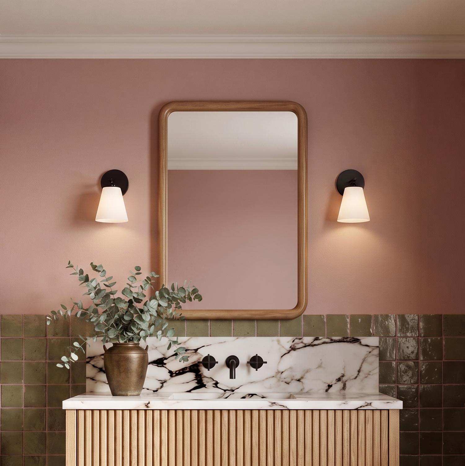 A modern bathroom with two matte black wall sconces with opal glass shades flanking a wood-framed mirror above a marble vanity and fluted wood cabinet.