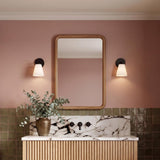 A modern bathroom with two matte black wall sconces with opal glass shades flanking a wood-framed mirror above a marble vanity and fluted wood cabinet.