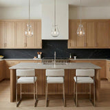 A transitional kitchen features three Emma Pendant Light 7", Polished Nickel glass fixtures over a marble island with light wood cabinetry and a black marble backsplash.