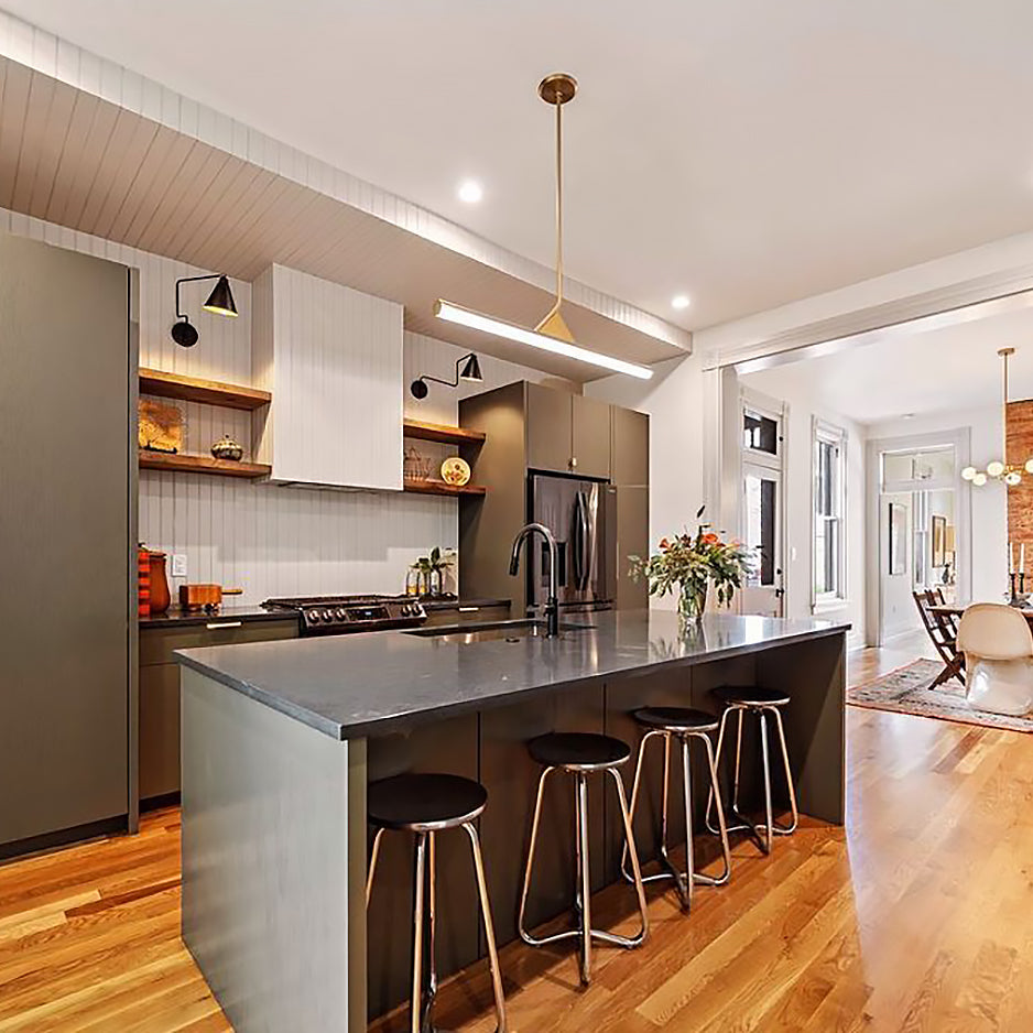 Customer photo of Argo Linear LED Pendant Light in Satin Brass, installed in a large, open-concept and modern kitchen. The light is hung above the island with four bar stools. 