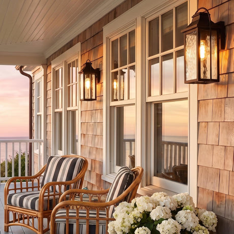 A coastal home porch featuring Preston Outdoor Wall Light, Small fixtures in oiled bronze glowing on cedar shake siding beside striped wicker chairs and white hydrangeas at sunset.