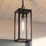 A modern farmhouse porch with the Sam Outdoor Hanging Light in matte black suspended from a white shiplap ceiling with a glowing Edison bulb at dusk.