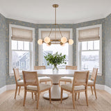 A coastal dining room featuring the Castell 6 Globe Round Chandelier 36 in Aged Brass over a white pedestal table with woven rattan chairs and blue wallpaper.