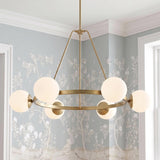 A transitional dining room featuring the Castell 6 Globe Round Chandelier 36", Aged Brass suspended before soft blue botanical wallpaper and white crown molding.
