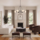 A contemporary living room with the Castell 6 Globe Round Chandelier 36", Matte Black featuring frosted glass globes centered above a marble coffee table and white sofa.