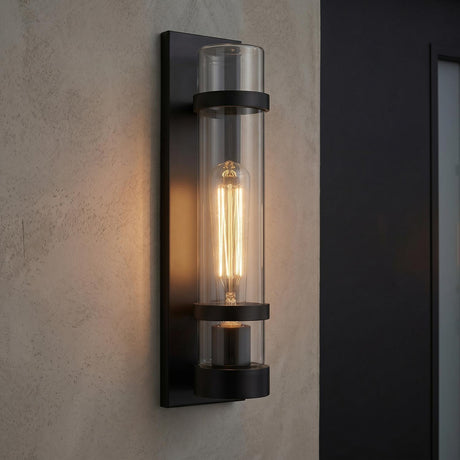 A modern outdoor entryway featuring the Glenn Outdoor Wall Light, Matte Black with a clear glass cylinder and filament bulb mounted on a textured beige wall.