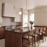 A transitional kitchen with the Milo 2 Globe Linear Arc Pendant 39", Aged Brass, over a dark marble island featuring walnut cabinetry and a vertical tile backsplash.