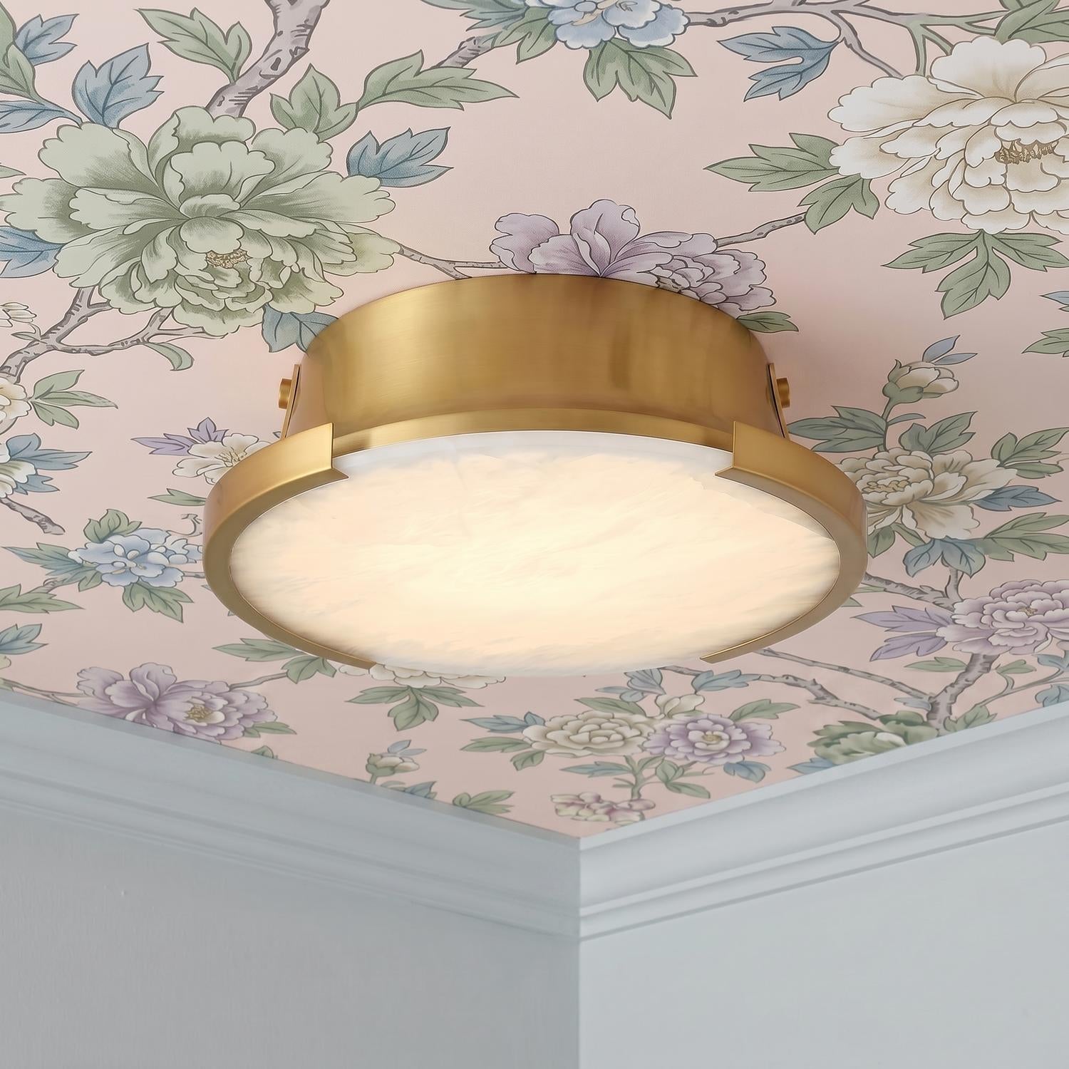 A transitional foyer featuring the Joni LED Alabaster Flush Mount 14 inch in aged brass installed along a ceiling with pink floral wallpaper and white crown molding.
