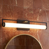 A contemporary bathroom with the Ian LED Vanity Light, Matte Black and Aged Brass, mounted over a circular gold mirror on a red marble tile wall.