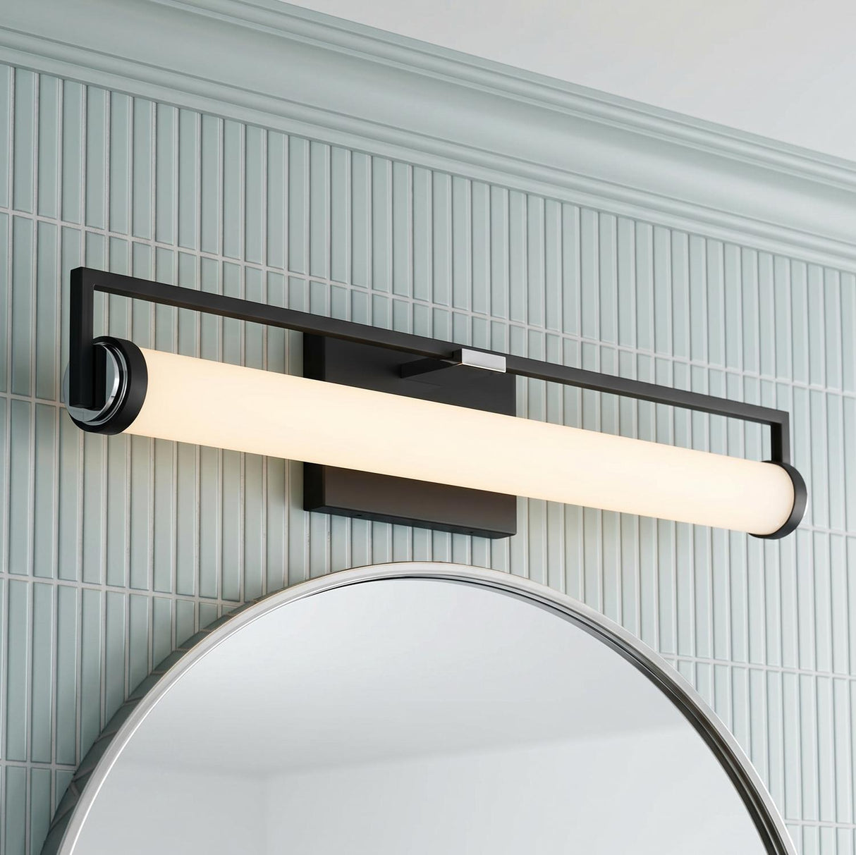A contemporary bathroom featuring the Ian LED Vanity Light, Matte Black and Chrome, mounted over a round mirror against light blue vertical tile with crown molding.