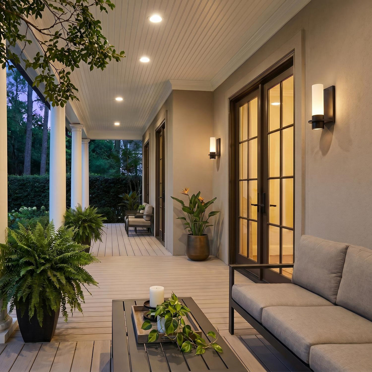 A transitional porch featuring two oiled bronze Luna LED Outdoor Wall Sconces flanking double glass doors on a stucco facade at twilight with potted ferns.