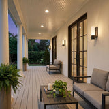 A Colonial porch with Luna LED Outdoor Wall Sconce fixtures in matte black flanking glass doors on white stucco at twilight, featuring gray decking and ferns.